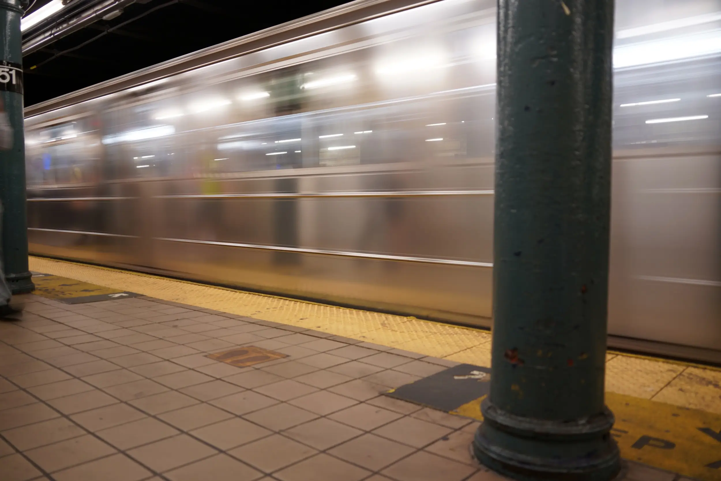 Metrotog i fart forbi perronen på en station i New Yorks subway