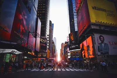 Times Square med store reklameskærme og fodgængere i fodgængerfeltet ved solnedgang